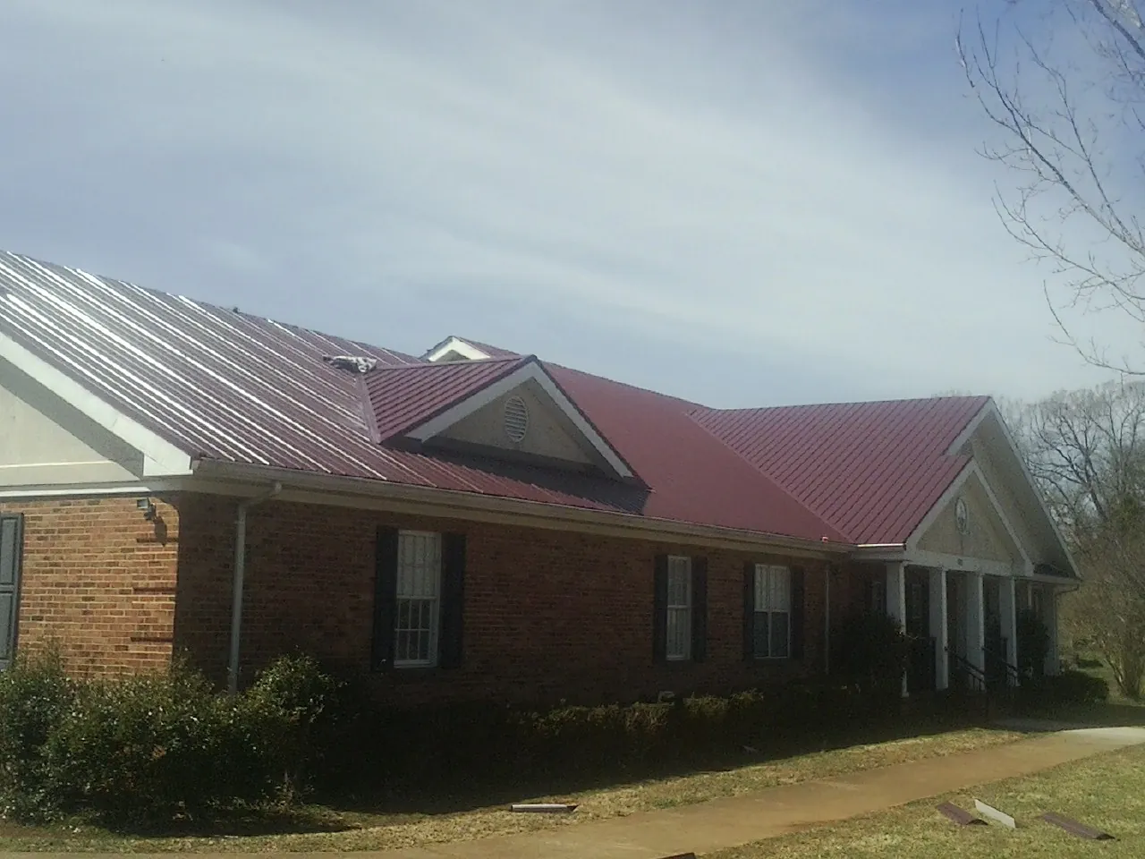 Red metal roof with gabled entries on a long brick building, from a Hail Damage Roof Repair job in Greenland