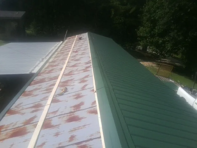 Old rusted panels beside newly installed green metal roofing — Wind Damage Roof Repair by Roofing Brothers in Greenland
