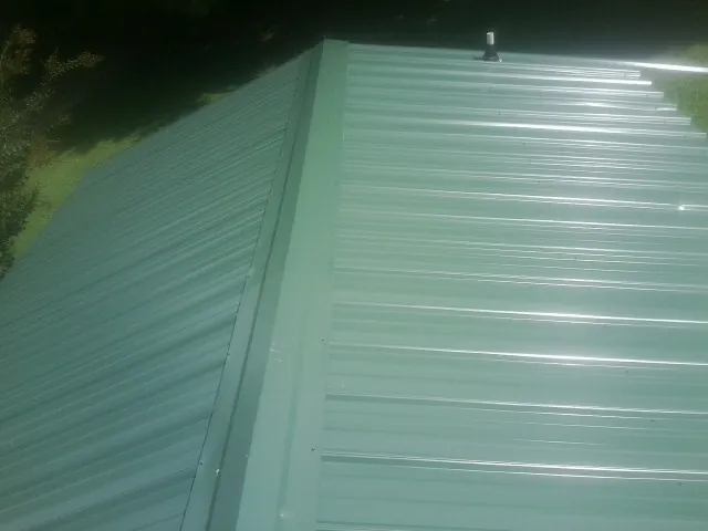 New green metal panels meeting at the ridge of a roof — Flat Roof Repair work by our crew in Greenland