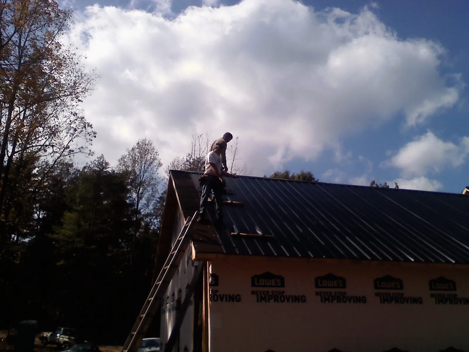 Roofer fastening dark metal panels high against a cloudy sky, from a Roof Inspection job in Greenland