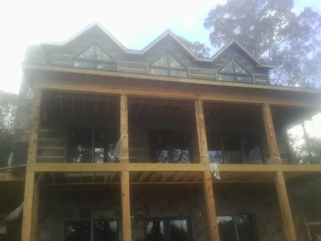 Dormers and porch framing on a large log home under construction — Roof Coating work by our crew in Greenland