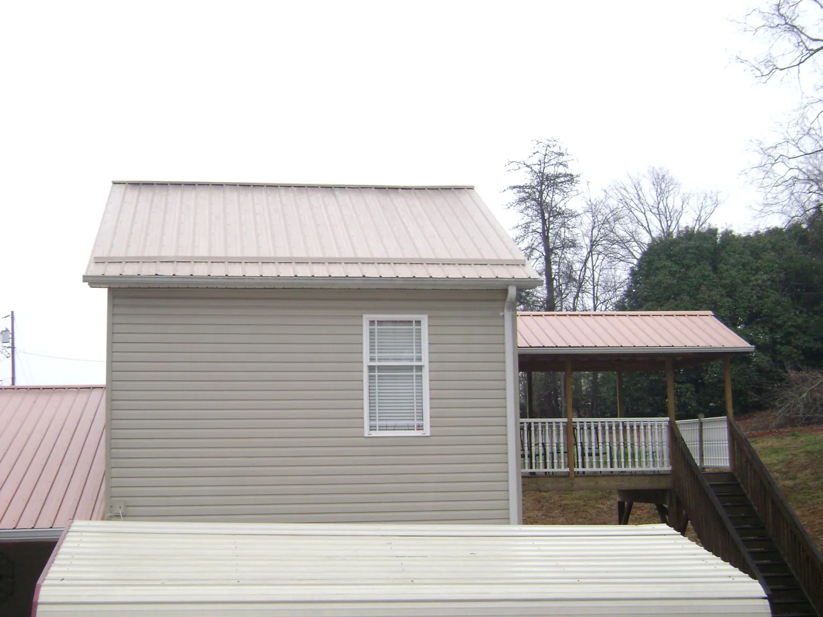 Tan metal roofs on a two story addition and attached porch, from a Roof Replacement job in Greenland
